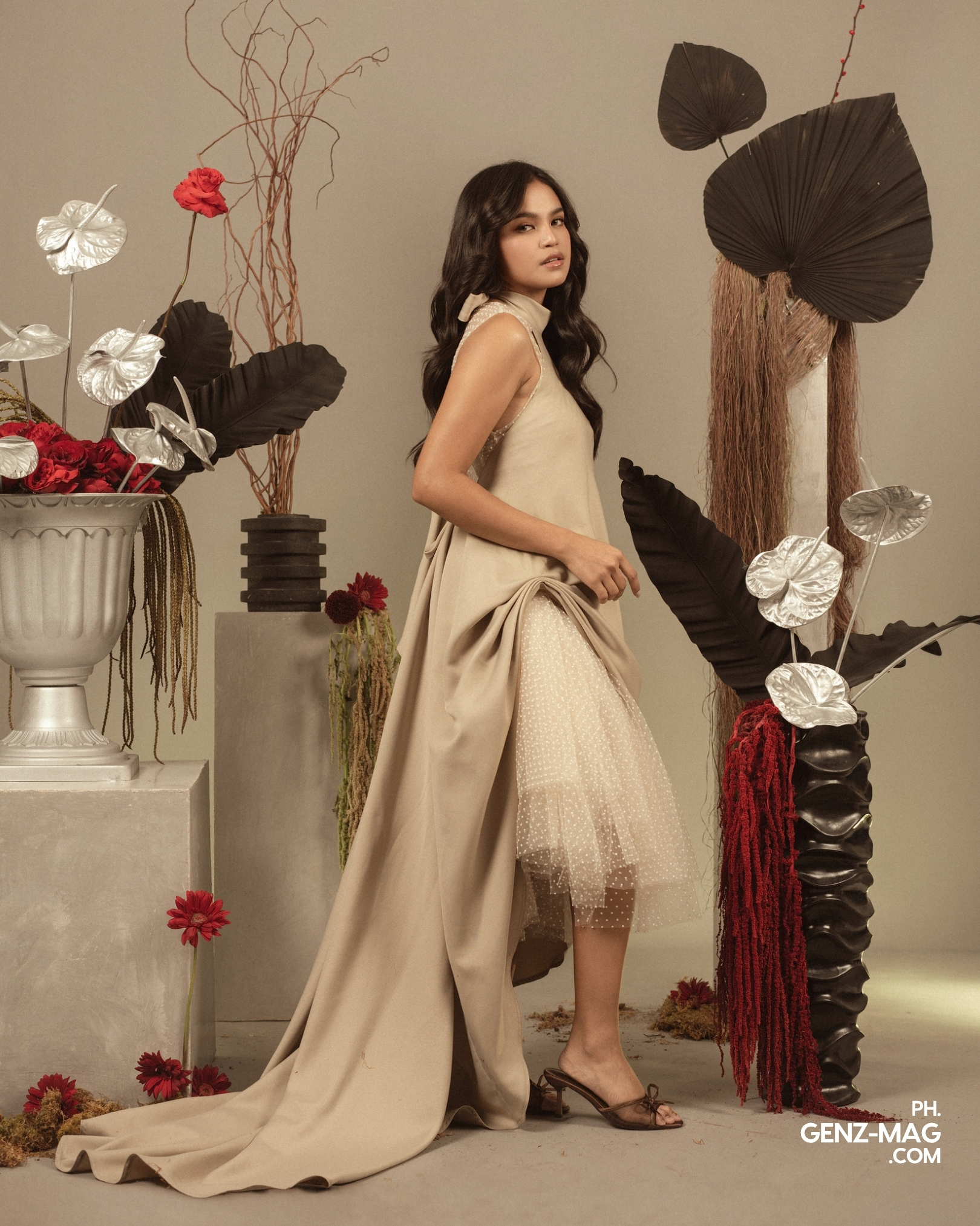 Alt text: "Zephanie in a draped beige gown over a polka-dot tulle skirt, standing among red rose and silver anthurium arrangements with floral styling by Makati Flower Atelier, for GEN Z Magazine's cover story with Michael Sager