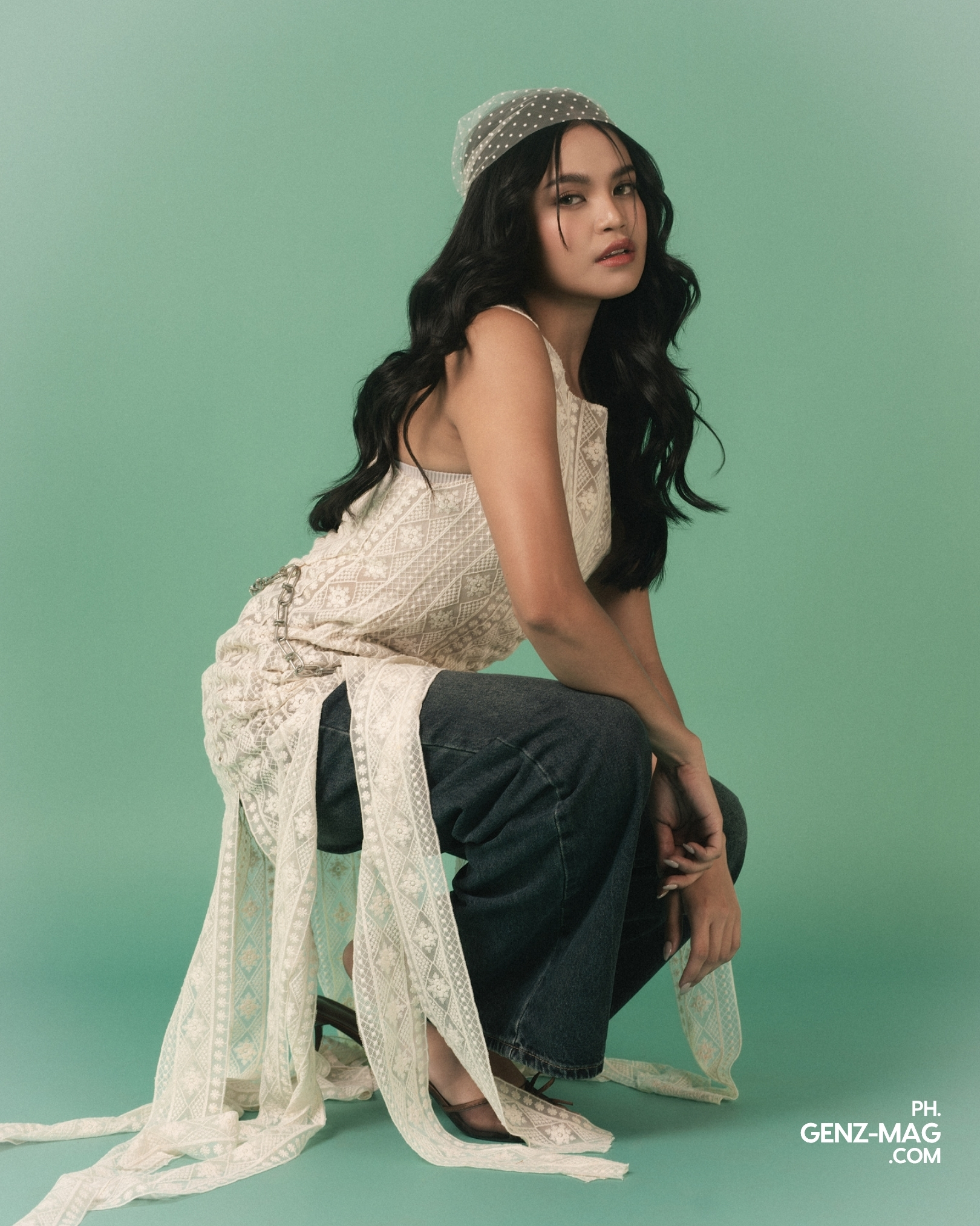 Zephanie crouched in a lace top and wide-leg denim with a polka-dot headscarf, against a sage green backdrop, for GEN Z Magazine's cover story with Michael Sager.