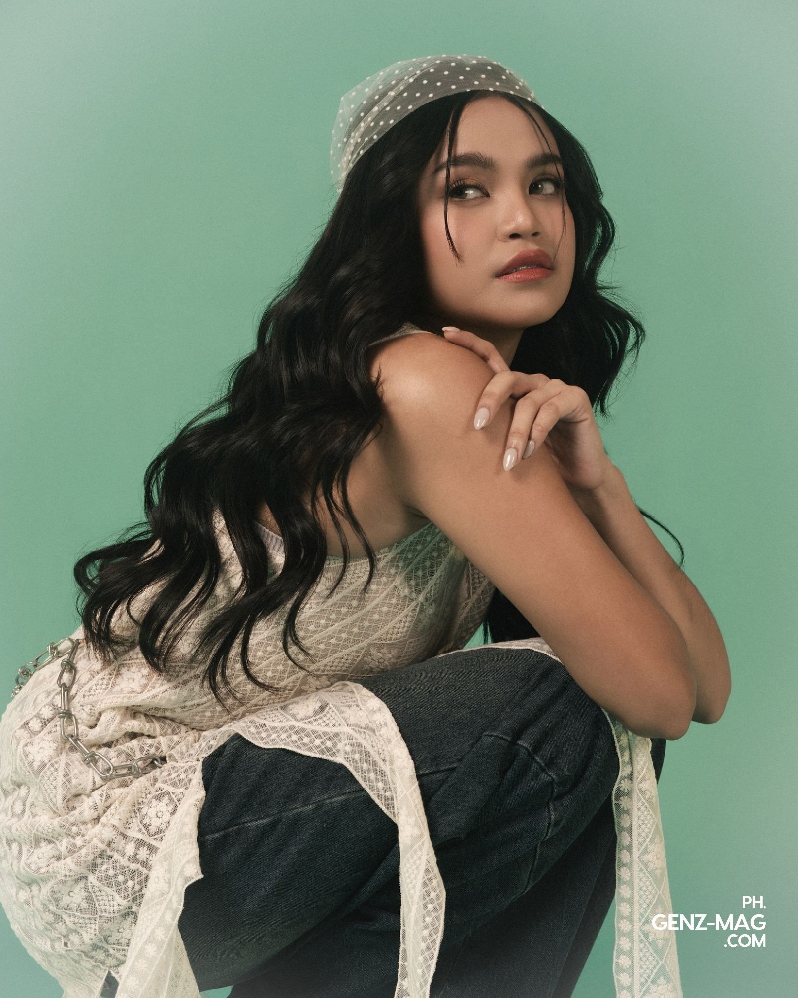 Zephanie glancing over her shoulder in a lace top and chain belt, resting her chin on her knee, for GEN Z Magazine's cover story with Michael Sager