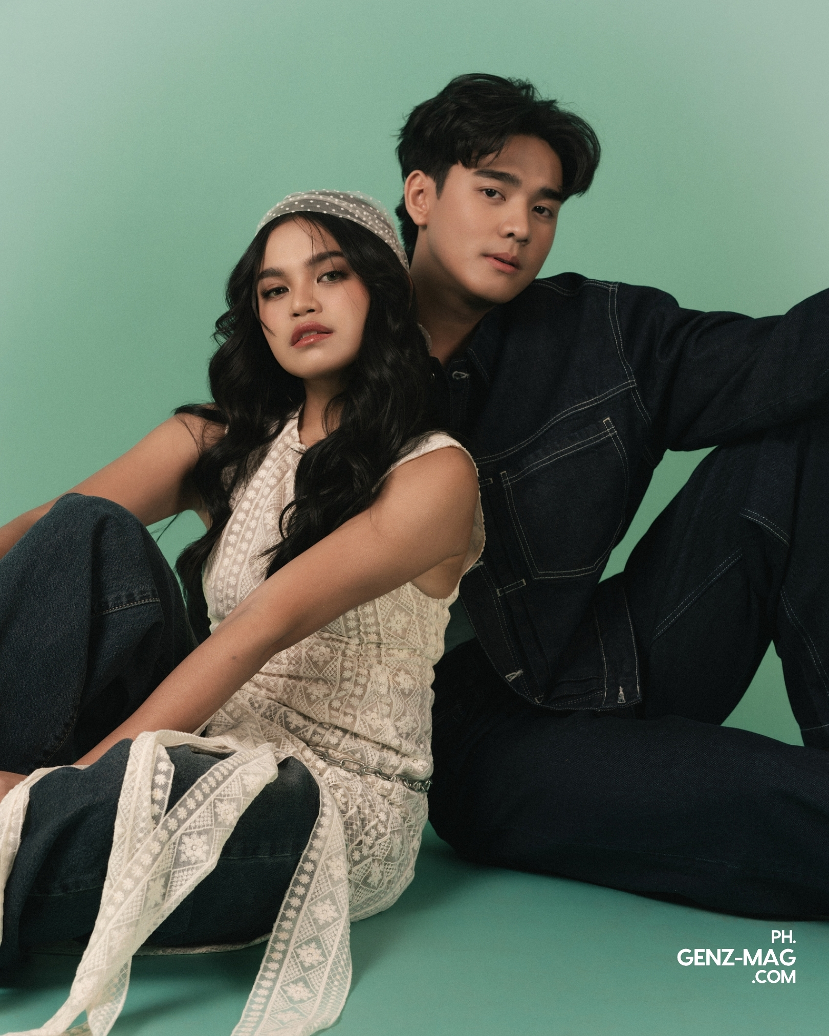 Zephanie and Michael Sager seated back to back on the floor, both in denim, facing the camera against a sage green backdrop, shot at The Villa Studios, for GEN Z Magazine's cover story