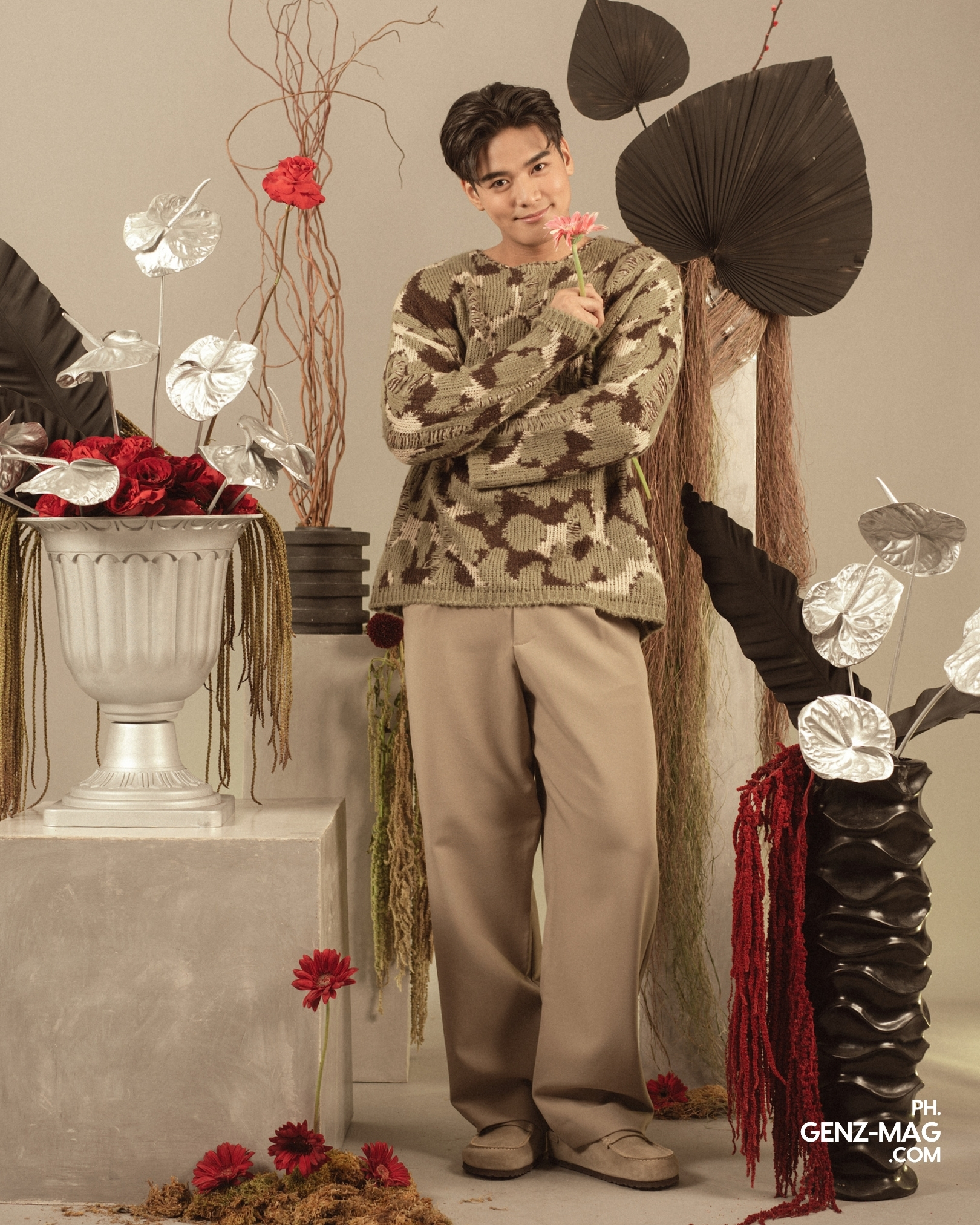 Alt text: "Michael Sager standing among red rose and silver anthurium arrangements, holding a pink gerbera daisy, with floral styling by Makati Flower Atelier, for GEN Z Magazine's cover story with Zephanie.