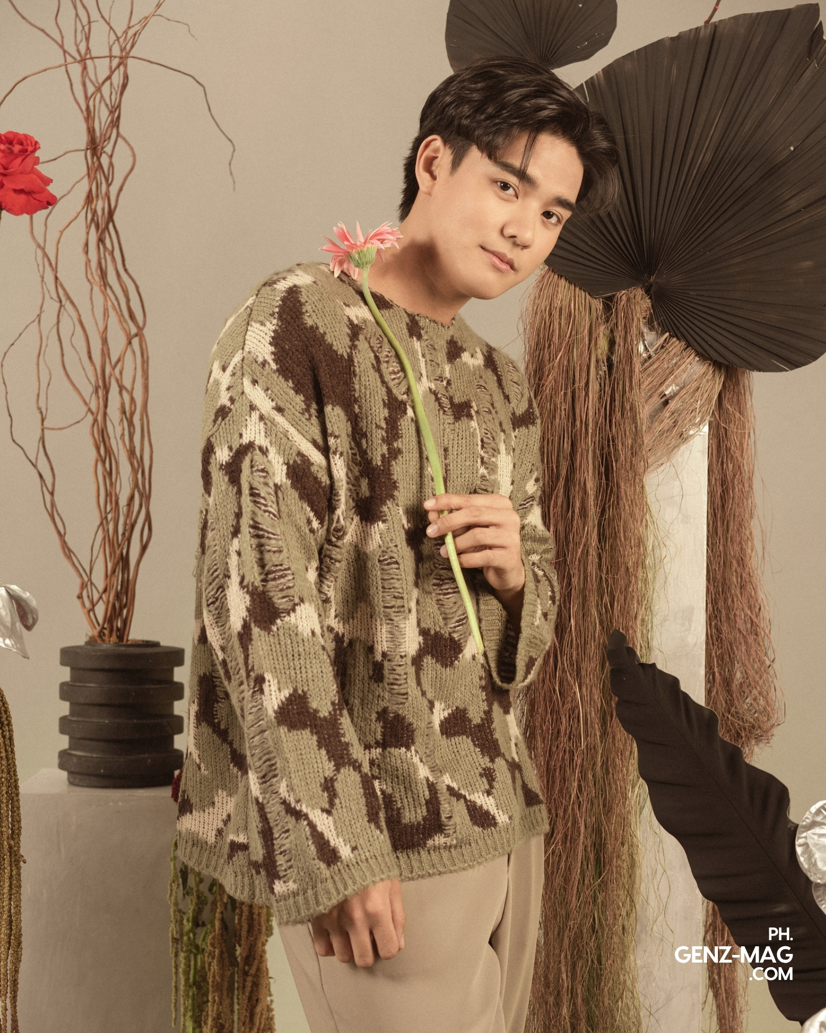 Michael Sager holding a pink gerbera daisy against his shoulder, leaning against dried floral decor by Makati Flower Atelier, for GEN Z Magazine's cover story with Zephanie.