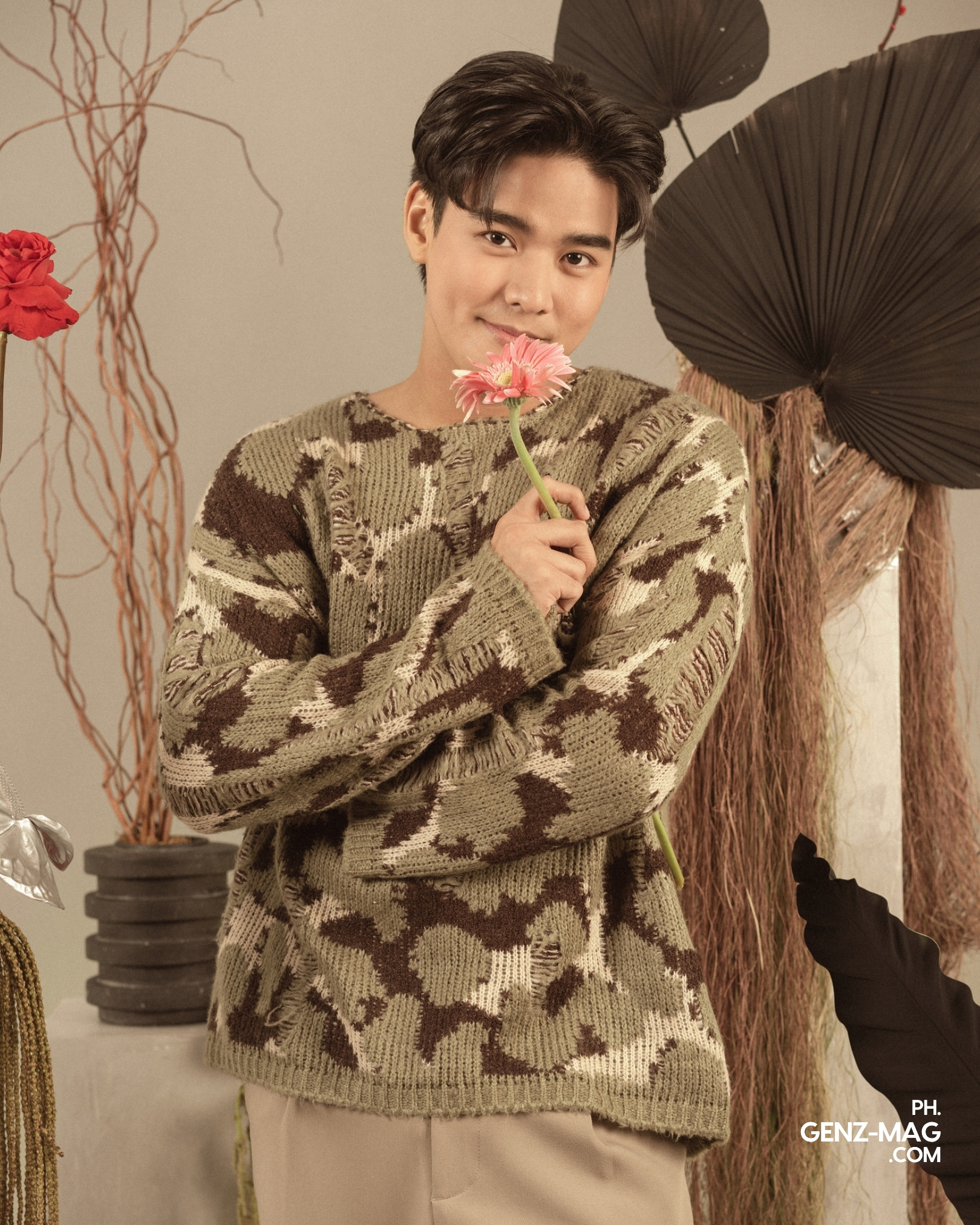 Michael Sager smelling a pink gerbera daisy while smiling at the camera, wearing a knit sweater, with floral styling by Makati Flower Atelier, for GEN Z Magazine's cover story with Zephanie.